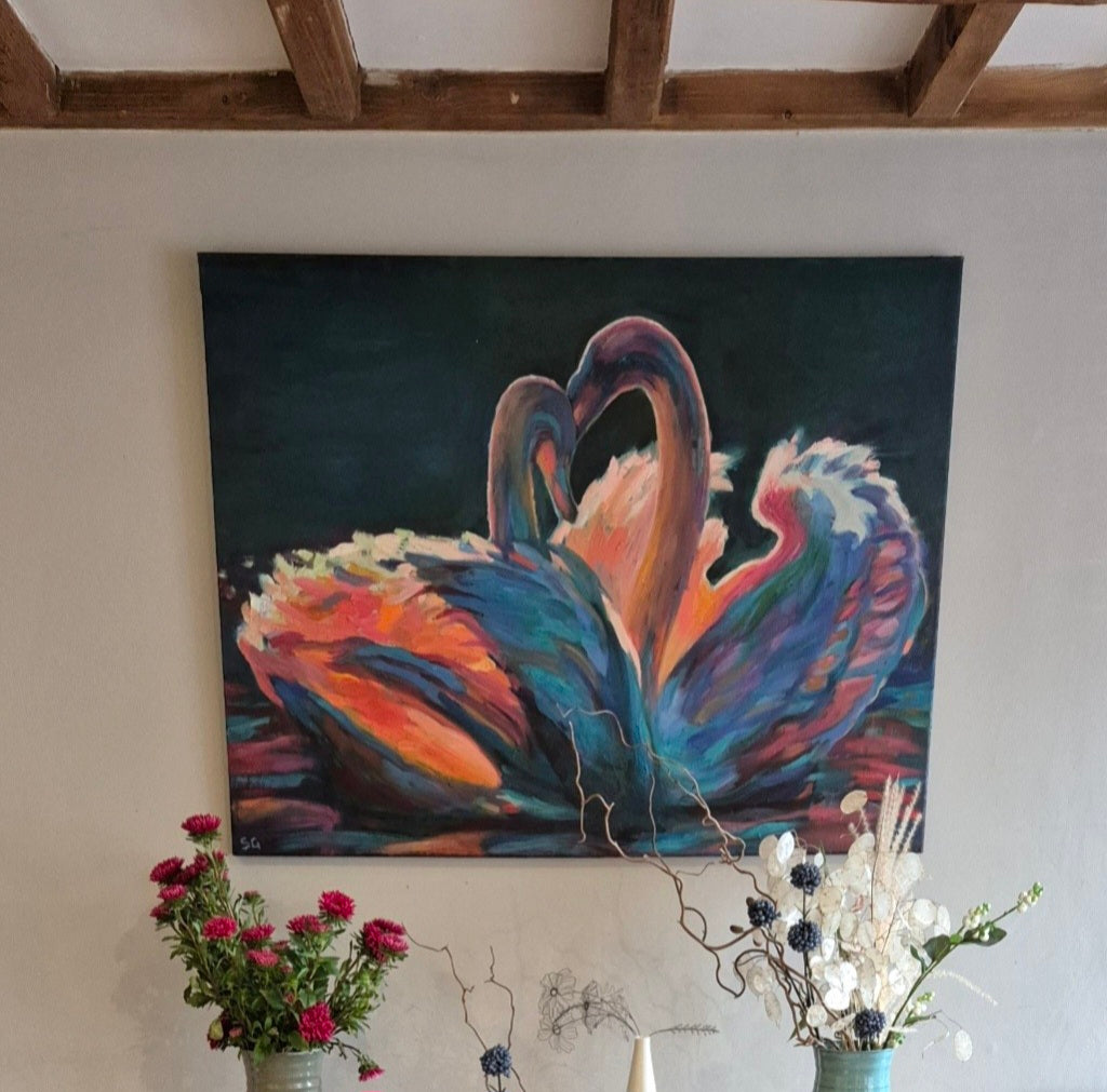 Colorful painting of two swans on a wall above a table with flowers and decorative items.
